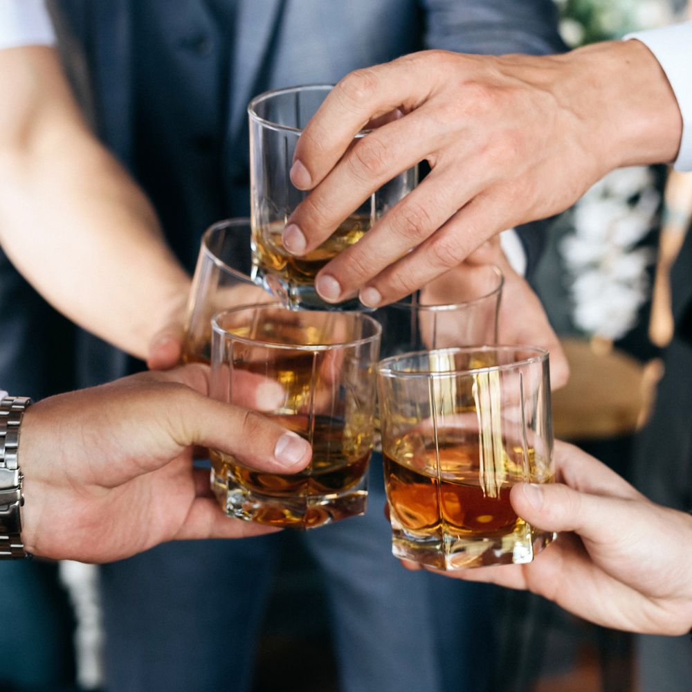 Osoby zbijają kieliszki z whisky na imprezie firmowej